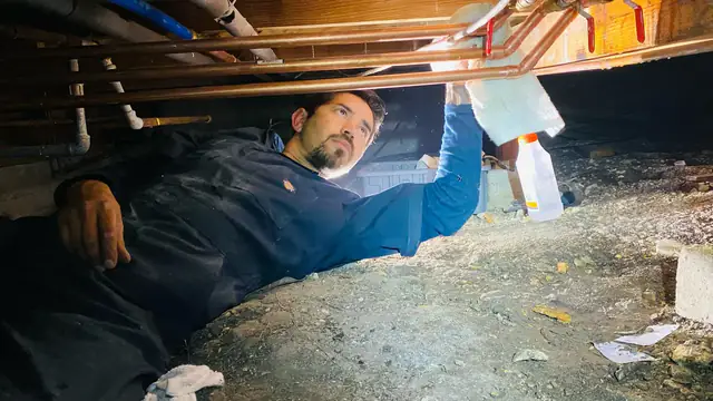 Victor lying in a crawlspace working on copper supply lines with a work light