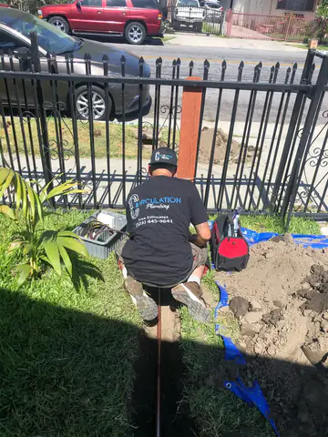 Victor in a Circulation Plumbing shirt kneeling beside a trench in a front yard for a new water line